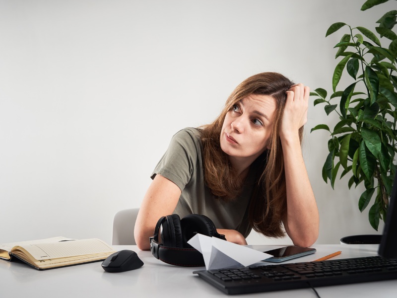 Find out what makes you procrastinate and eliminate it! A woman sitting in front of a desk procrastinating.
