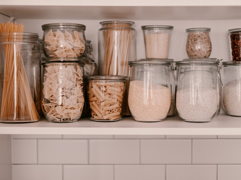 Organized food pantry shelf with transparent storage containers for pasta and cereal products. Organized food pantry shelf with transparent storage containers for pasta and cereal products.