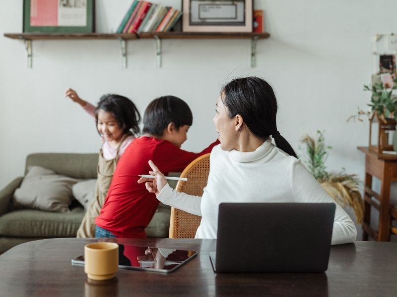To increase productivity, keep distractions at bay! A woman working on a laptop has turned around to scold two children who are causing distraction behind her.